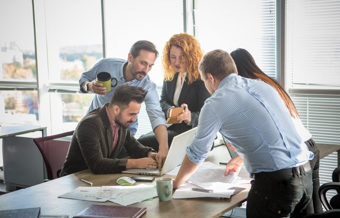 Business people showing team work while working in board room in office interior. People helping one of their colleague to finish new business plan. Business concept. Team work.